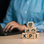 Bild von Holzklötze mit KPI drauf und drei flächen mit einer person an einem Laptop